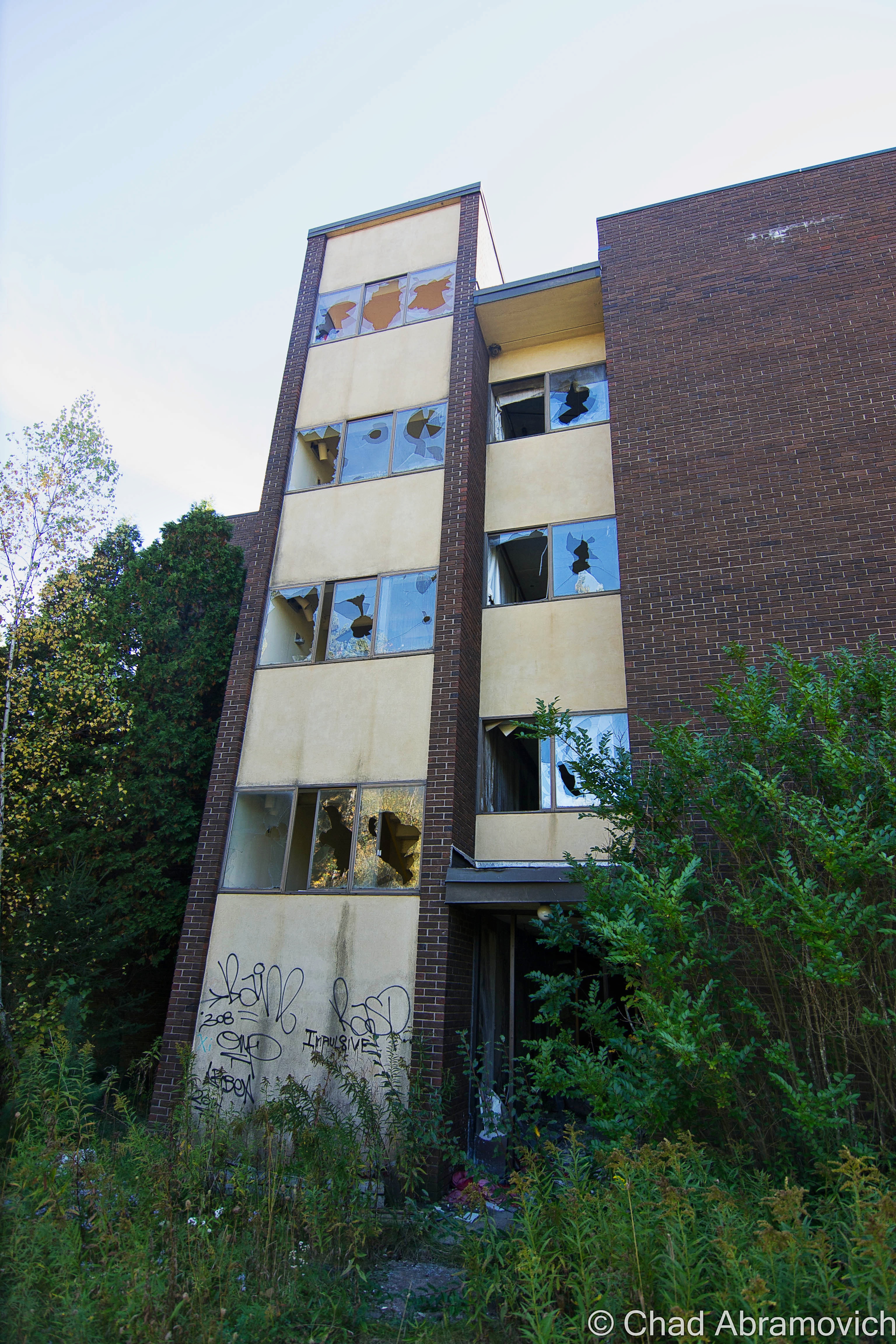 The eeriness of the property was unshakable as I walked around. The ugly and dated buildings were reduced to indignant and unsettling billboards that reckless destruction wrote. All the windows were broken, the doors and walls kicked in. A fetid stench was the first thing I noticed long before I tromped under the coolness of the building shadows, a stagnant foul entity that permeated around the entire property. 